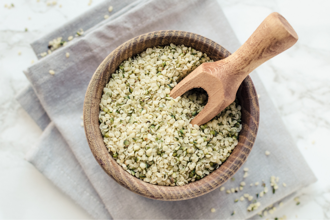 wooden bowl of hemp seed hearts with a wooden spoon on top of a grey tea towel