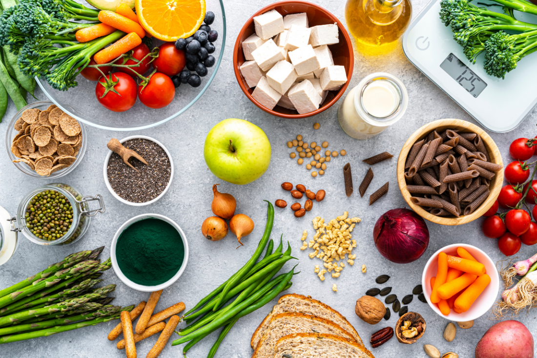 different types of colourful plant based foods with a weighing scale on a grey background