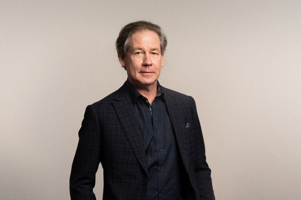 iüLabs Doctor Bob McDonald in a black suit and shirt, with a natural grey background
