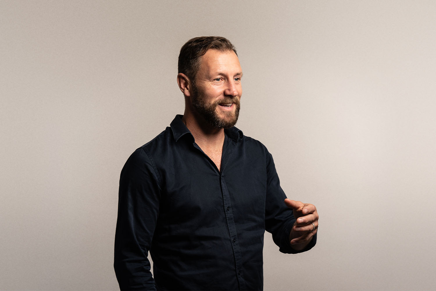 iüLabs Carlyle Jenkins talking and smiling, wearing a black shirt, with brown hair and a natural grey background